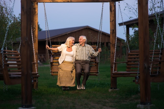 An elderly couple sitting on a porch swing, smiling at each other, with a serene garden in the background, representing a peaceful retirement.