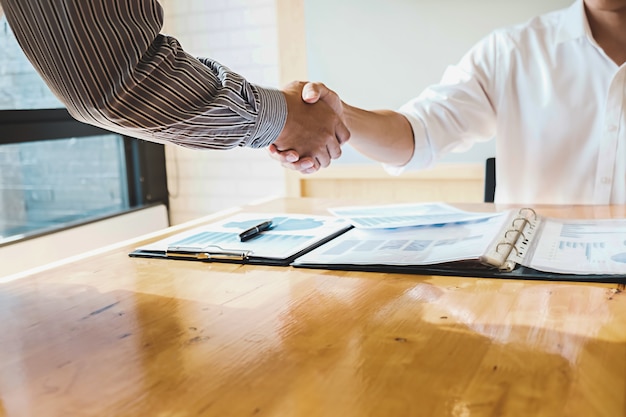 A close-up shot of a professional shaking hands with their client over a neat desk with a finance plan on it.