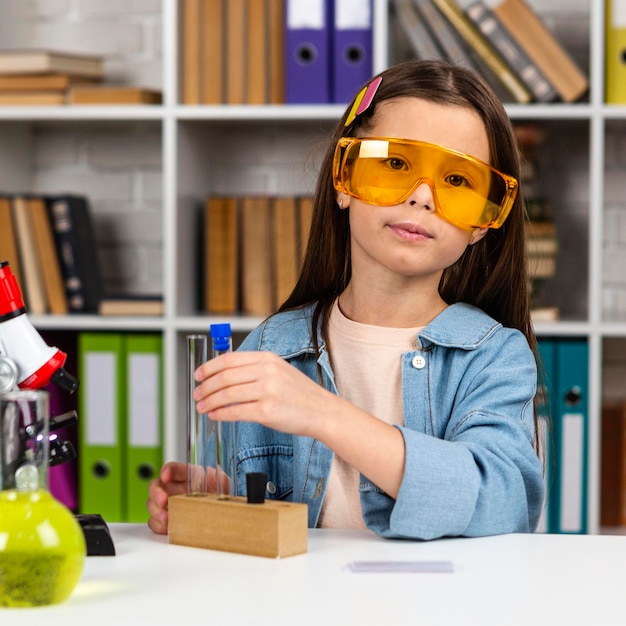 A young girl, wearing safety glasses, excitedly examines a complex circuit board in a science lab. Her expression is one of curiosity and discovery, highlighting the impact of hands-on STEM learning.