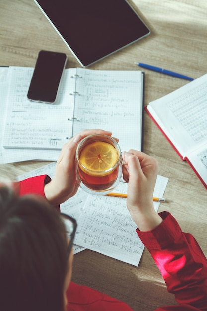A close-up shot of a student thoughtfully writing their college application essay at a desk filled with books and notes. A cup of coffee sits nearby. The student's brow is furrowed in concentration.