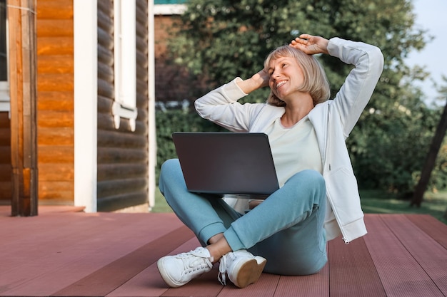 A person smiling while sitting outside with a laptop, representing the increased financial freedom and flexibility from financial minimalism.