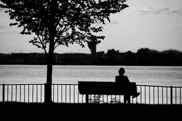 A silhouette of a person sitting on a park bench, looking thoughtful, with a subtle graphic overlay of supportive hands reaching out from the sides. The image evokes feelings of confidentiality, support, and access to help.