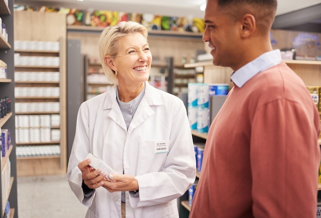 A pharmacist handing a prescription to a customer over the counter. Both are smiling and engaging in a friendly conversation. The pharmacy is well-lit and organized, with various medications and health products in the background.
