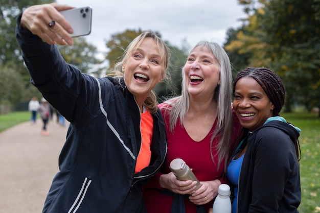 A group of employees playfully participating in a walking challenge. The setting is an outdoor park with trees and sunny weather. Some are using fitness trackers, and others are laughing and chatting.